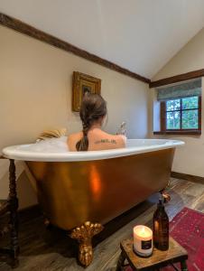 une femme assise dans une baignoire en cuivre dans une pièce dans l'établissement Romantic Country Cottage with log burner, garden patio, outdoor tub and country views- Brecon Beacons National Park, à Llangadog