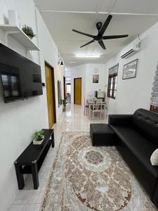 a living room with a black couch and a ceiling fan at Santai DPermai Homestay in Selama