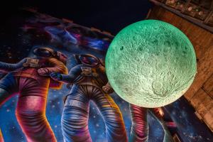 ブダペストにあるJO&JOE Budapestの緑の惑星を抱えた3人の宇宙飛行士の絵