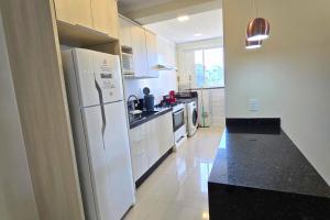 a kitchen with a white refrigerator and a black counter top at Apartamento no Coração de Bombinhas in Bombinhas