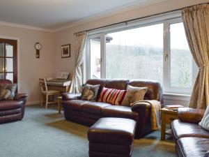a living room with a leather couch and a large window at Tigh Raineach in Strathyre