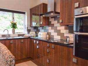 Una cocina con armarios de madera y un fregadero y una ventana. en Beudy-Oh2, en Dihewid