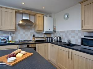 a kitchen with wooden cabinets and a cutting board with cheese at 1 Harbour View in Newquay +9 photos