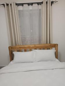 a bed with white pillows in front of a window at 1 bedroom BNB Meru in Meru