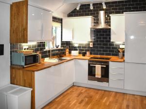 una cucina con armadietti bianchi e una parete di piastrelle nere di Fawns Cottage a Culmstock