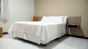 a bedroom with a bed with white sheets and pillows at Pousada Colonial in Macaé