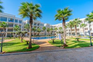 a large apartment building with palm trees and a pool at Spacious luxury apartment with pool in Bouznika