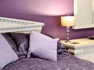 a bed with purple walls and a table with a lamp at Stable Cottage in Penrhyn Bay