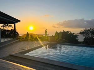 a swimming pool with a sunset in the background at Lodge Orchidée de la Villa La Palmira - Vue Mer - Jacuzzi Privé - Accès Piscine - Lit King Size - Clim - 4 étoiles - Proche commodités - TV - connectée - Internet fibre - Proche Plage in Les Anses-dʼArlets
