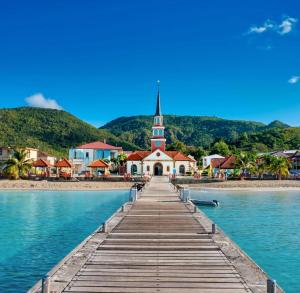 a dock leading to a church with a church steeple at Lodge Orchidée de la Villa La Palmira - Vue Mer - Jacuzzi Privé - Accès Piscine - Lit King Size - Clim - 4 étoiles - Proche commodités - TV - connectée - Internet fibre - Proche Plage in Les Anses-dʼArlets