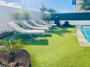 a row of lounge chairs on a lawn next to a pool at Villa Neo - Private Pool - 8 minutes Corralejo, mini Gym!! in Villaverde