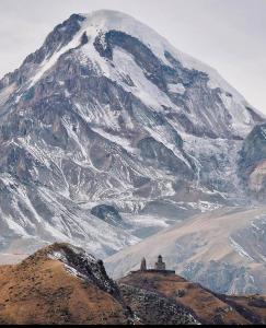 Una montaña cubierta de nieve con un edificio delante. en Edelweiss cottage Kazbegi, en Kazbegi