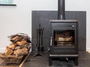 een zwarte kachel met een mand houtblokken bij Willow Barn - Fernhill Farm in Wootton Bridge