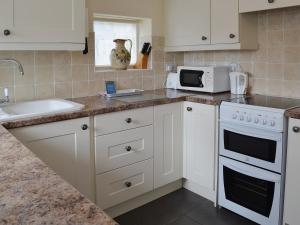a kitchen with white cabinets and a sink and a microwave at Rockville Cottage - 24376 in Bempton