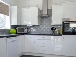 a white kitchen with white cabinets and a microwave at Wayside Cottage in Brigham