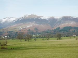 a field with snow covered mountains in the background at Acorn Lodge - Burnside Park in Keswick