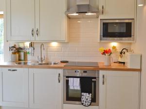 a kitchen with white cabinets and a sink and a stove at Fig Cottage in Brabourne
