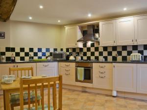 a kitchen with white cabinets and a table and a stove at Shippon Cottage - E4299A in Halston