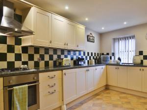 a kitchen with white cabinets and black and white tiles at Shippon Cottage - E4299A in Halston +4 photos