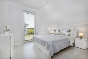a white bedroom with a bed and a window at Domki apartamentowe Na wrzosach in Jastrzębia Góra
