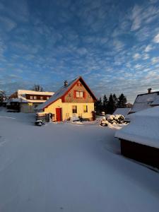 a house with snow on the ground next to buildings at Chaloupka Příchovice in Kořenov