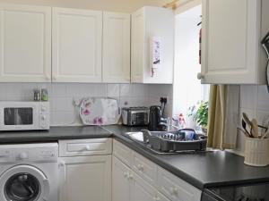 a white kitchen with a sink and a microwave at Ivy Cottage in Henllan