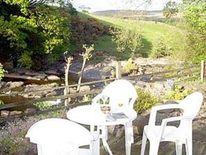 three white chairs and a table with a view of a hill at 2 Farfield Cottages in Sedbergh
