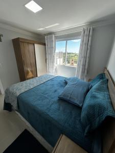 ein Schlafzimmer mit einem Bett mit blauer Bettdecke und einem Fenster in der Unterkunft AP Novinho! à 150m das piscinas! 3 ar cond - churrasqueira in Piratuba