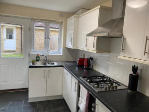 eine Küche mit weißen Schränken und einem Herd mit Backofen in der Unterkunft Warm & Cosy 4 Bed Cambridge House w Parking Garden & High Speed WIFI in Milton