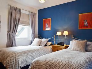 two beds in a room with blue walls and a window at 9 Howrah's Court in Keswick