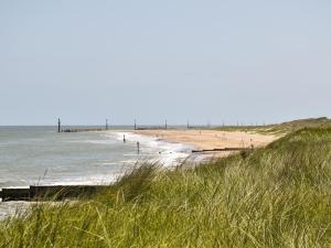 a beach with people in the water and grass at Hempstead End in Lessingham +2 photos