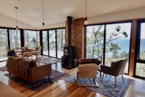 a living room with a table and chairs and windows at The Lookout House at Pirates Bay in Eaglehawk Neck