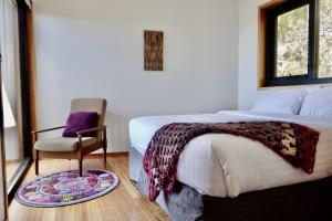 a bedroom with a bed and a chair and a window at The Lookout House at Pirates Bay in Eaglehawk Neck