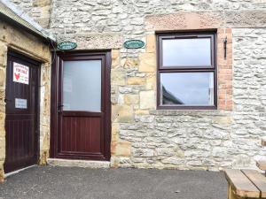 a stone building with two windows and a wooden door at Lathkill Cottage in Bakewell