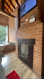 a living room with a brick fireplace with a tv at Chales Estância Verdejante in Sapucaí-Mirim +53 photos