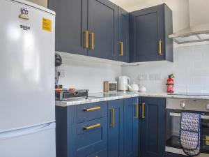 a kitchen with blue cabinets and a white refrigerator at Seashell House in Burnham on Sea +14 photos