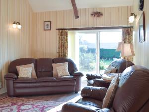 ein Wohnzimmer mit einem Ledersofa und einem Fenster in der Unterkunft Carthouse Cottage in Carew