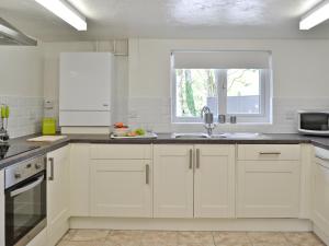 a white kitchen with white cabinets and a window at The Lodge - 29794 in Swimbridge