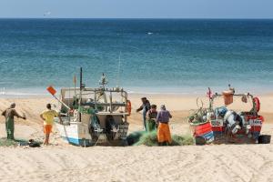 a group of people standing on a beach with a boat at NAU Salema Beach Village in Salema