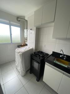 Una cocina blanca con estufa y fregadero. en Residencial Dalí, en Duque de Caxias