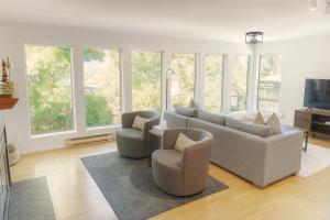 a living room with a couch and chairs and windows at Tonquin Beach House - EV Charger, Wood Fireplace, Steps from beach in Tofino
