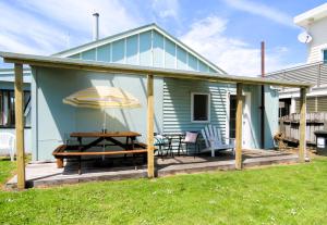 ein Haus mit einer Terrasse mit einem Tisch und einem Sonnenschirm in der Unterkunft CROOKED MILE COTTAGE - BY THE SEA - family friendly in Hokitika