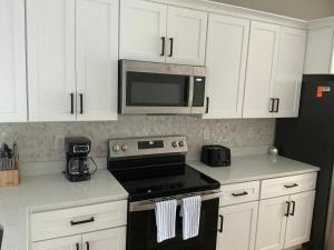 eine Küche mit weißen Schränken, einem Herd und einer Mikrowelle in der Unterkunft Orlando Luxury Home in Orlando