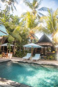 a pool with chairs and umbrellas and palm trees at Villa Tahid in Gili Islands