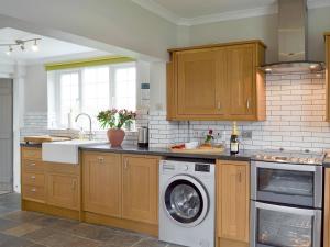 a kitchen with wooden cabinets and a washing machine at Holly Cottage in Pett