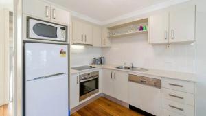 une cuisine blanche avec un réfrigérateur et un micro-ondes dans l'établissement Seaspray Breeze, à Yamba