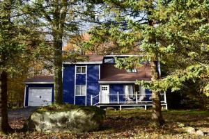 une maison bleue avec une terrasse couverte dans les bois dans l'établissement Pocono Mountain Chalet, à Tobyhanna