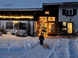 een kind dat met een slee door de sneeuw voor een huis loopt bij Am Hof Jungholz in Jungholz