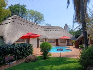 a house with a thatched roof and a swimming pool at Fortunesgate Lodge in Bulawayo