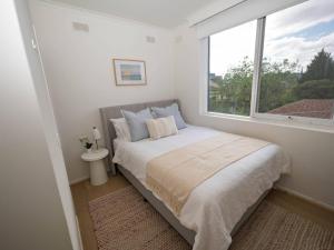 a white bedroom with a bed and a window at Villa Amari - A Sunny Tranquil Home in Melbourne